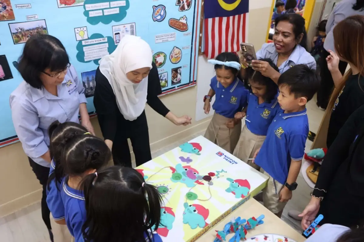 Children engaging in a fun educational activity using a Nippon Paint branded game, surrounded by teachers and parents in a colorful classroom setting.